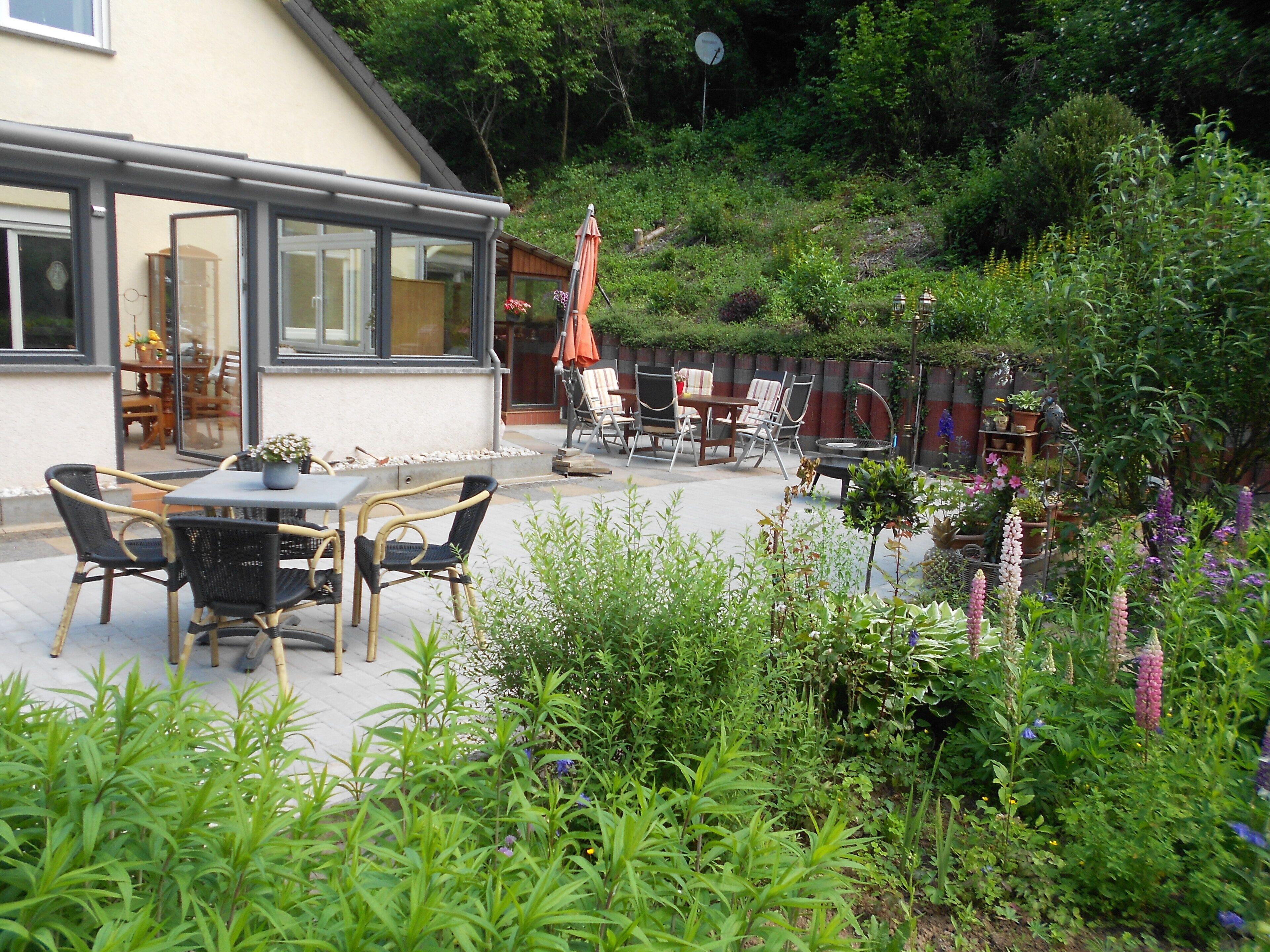 An outdoor patio area with a table and chairs, surrounded by lush greenery and various plants.