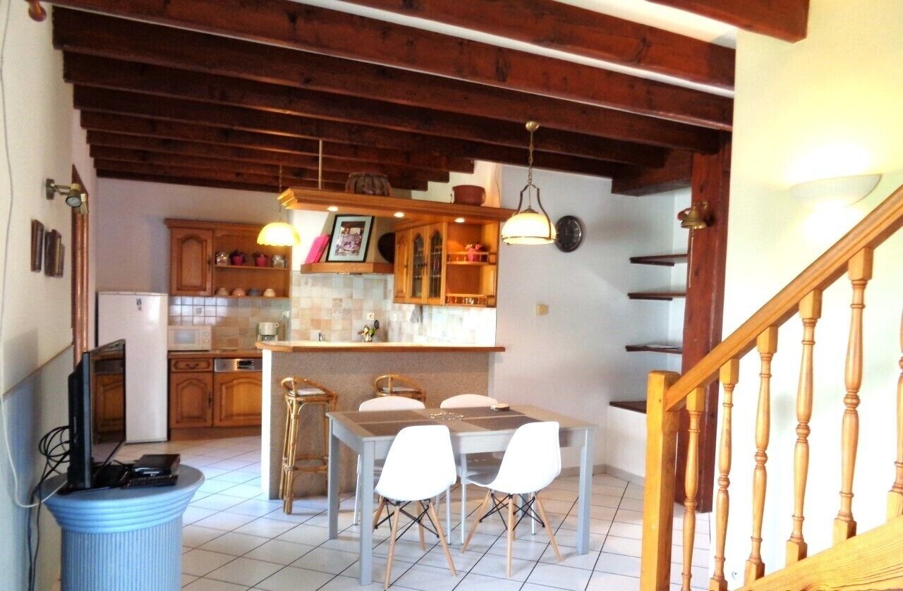 Una cocina con vigas de madera, una mesa de comedor con sillas y una escalera.