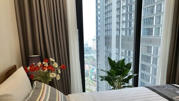 Une chambre d’hôtel avec un grand lit, une plante en pot et une vue sur le paysage urbain par la fenêtre.