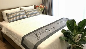 Un lit bien fait, agrémenté d’oreillers à rayures, d’un couvre-lit décoratif et d’une plante en pot placée à côté.