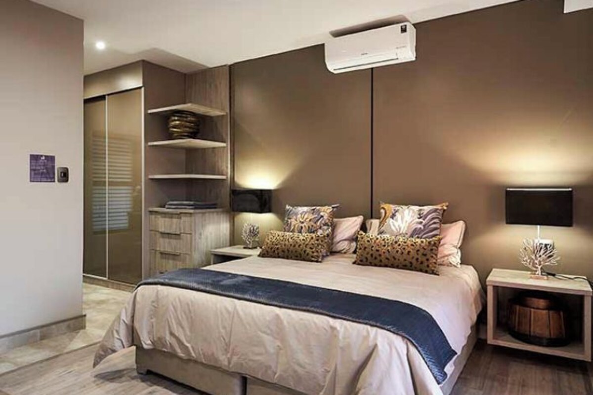 A modern bedroom with a large bed, built-in shelving, and a ceiling-mounted air conditioner.
