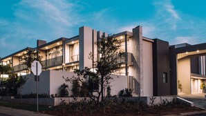 Un moderno edificio residencial de varios pisos con balcones, entrada para vehículos y jardines ajardinados.