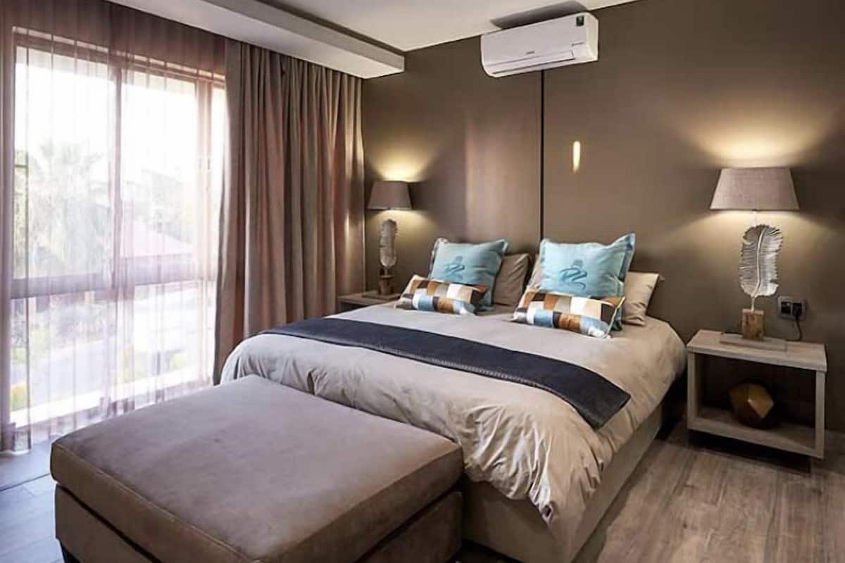 Une chambre moderne avec un grand lit, une table de chevet, un appareil de climatisation et une vue sur l’extérieur.
