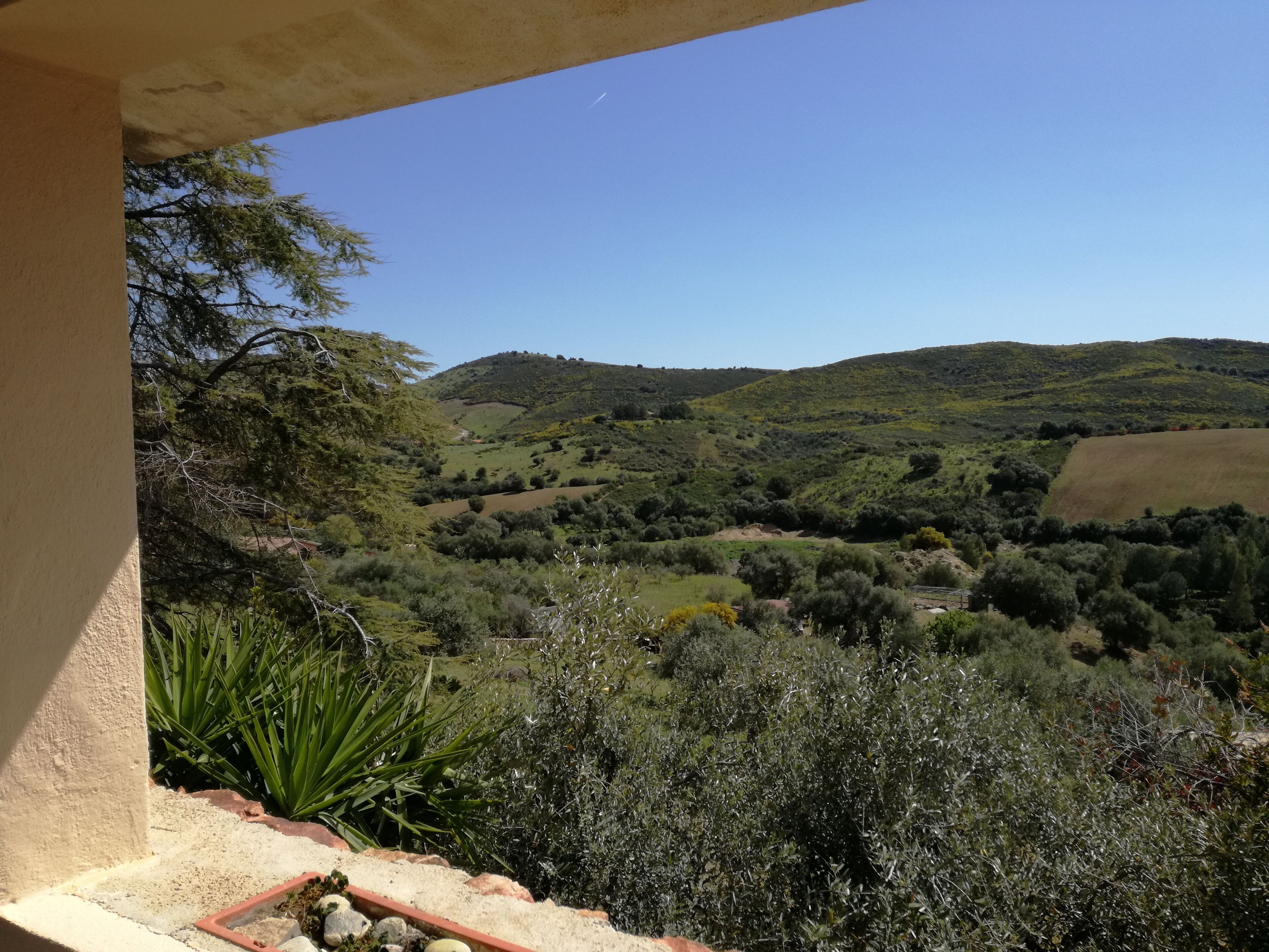 A balcony with a view of a hilly landscape, including trees and a clear sky.