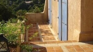 A building with a terracotta tiled patio, blue shutters, and a view of a hilly landscape. - Villa with swimming pool in the Gulf of SAINT-TROPEZ (La Croix-Valmer)