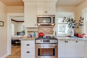 A kitchen with white cabinets, a stainless steel stove, a microwave, and a brick backsplash.
