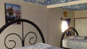 A room with two beds, one with a white mattress and the other with a floral-patterned one. There is a painting of sunflowers on the wall, and a ceiling with a blue and white swirling pattern. - Hostal Brisas y Olas - Hostel (San Juan del Sur)