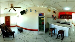 A room with a ceiling fan, a sofa, a kitchenette, and a bar area. - Hostal Brisas y Olas - Hostel (San Juan del Sur)