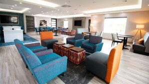 A modern hotel lobby with a mix of seating areas, a flat-screen TV mounted on the wall, and a dining area with tables and chairs. - Hotel Pryor (Pryor)