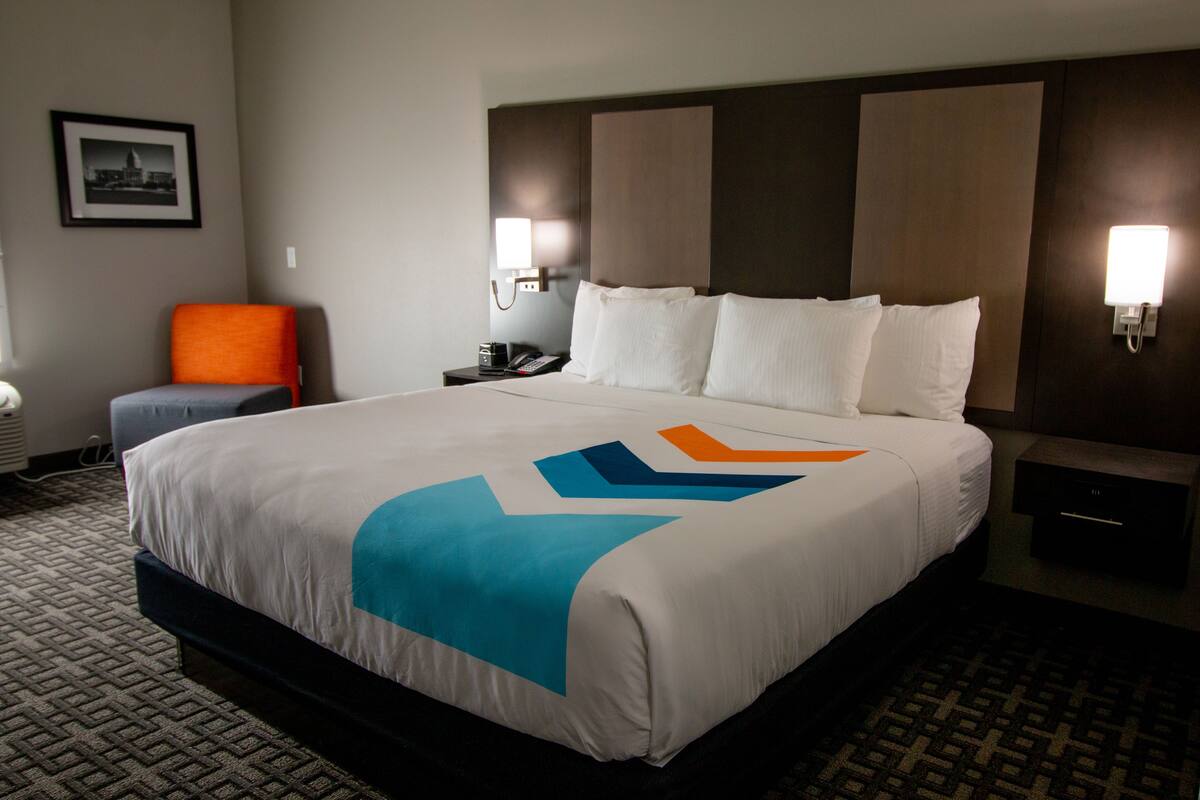 Habitación de hotel con una cama grande, una silla, una mesita de noche y una lámpara fijada a la pared.