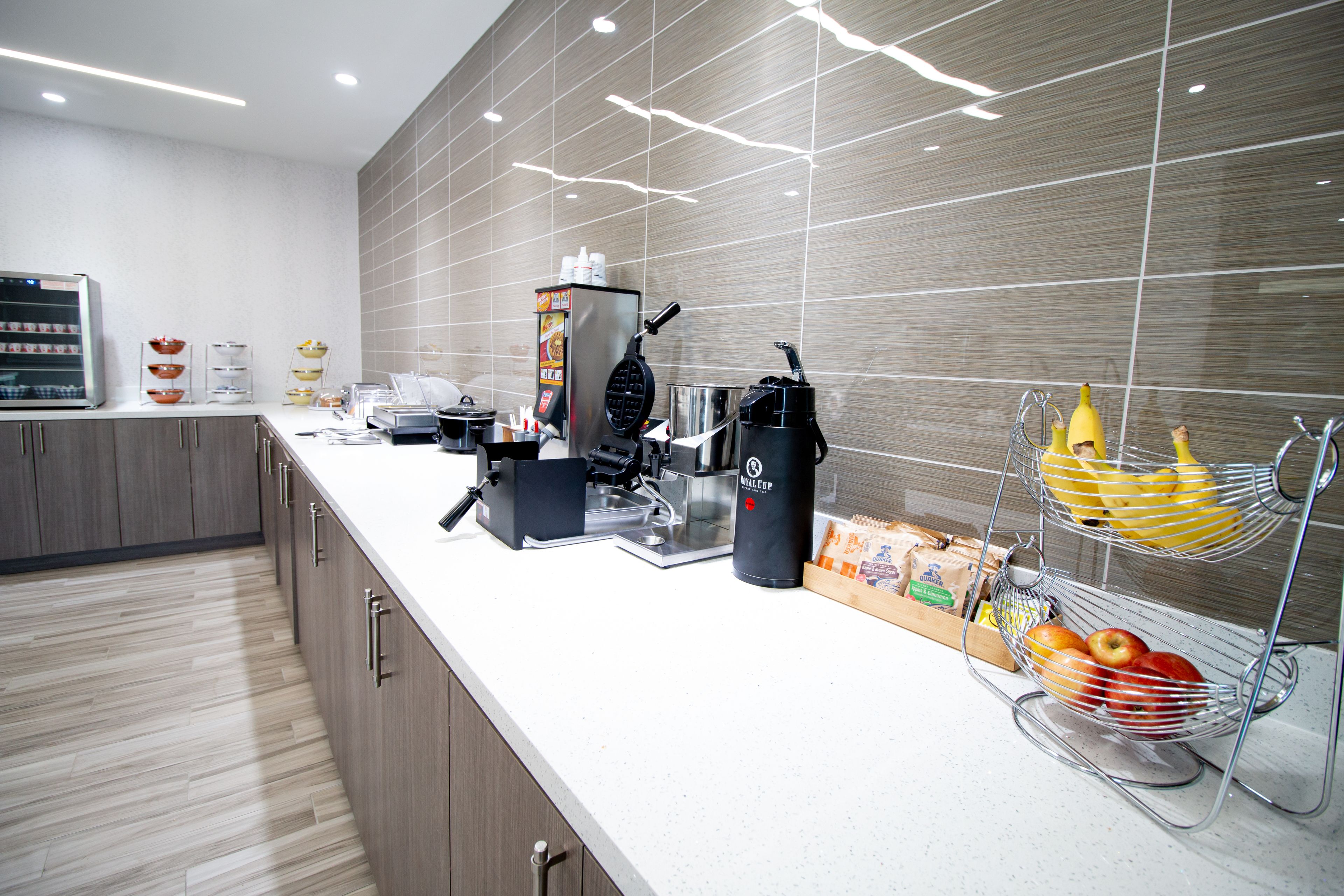 A modern kitchen with a coffee machine, a waffle maker, and a fruit basket.