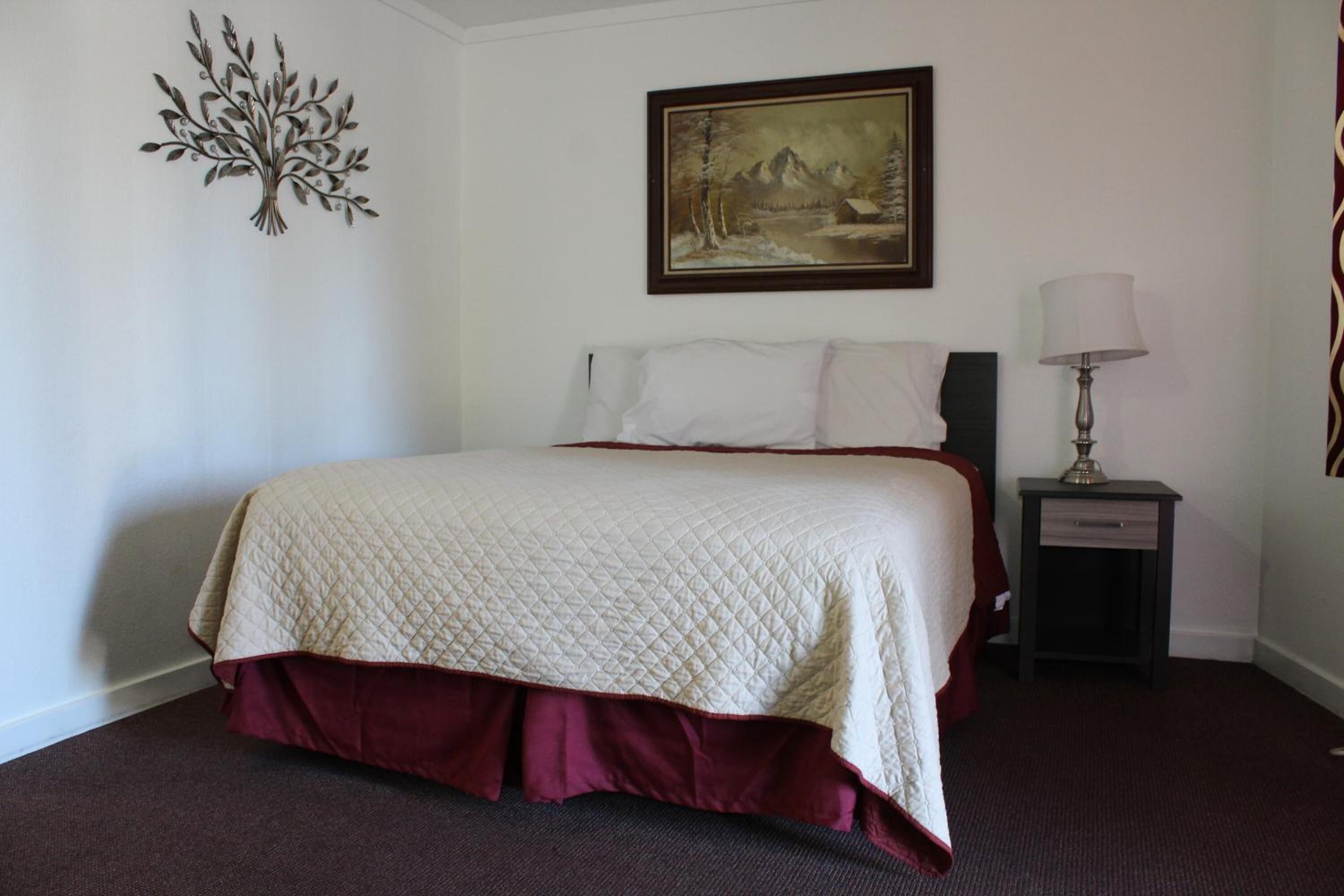 Uma cama bem arrumada com cobertura acolchoada, um quadro na parede acima e um abajur em uma mesa de cabeceira.