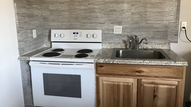 Una cocina compacta con estufa integrada, un lavamanos y armarios de madera.