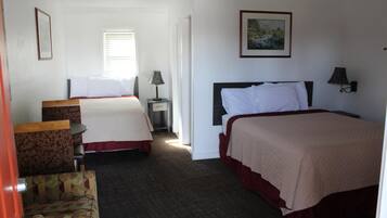 Habitación de hotel con dos camas, una mesita, una silla y un cuadro en la pared.