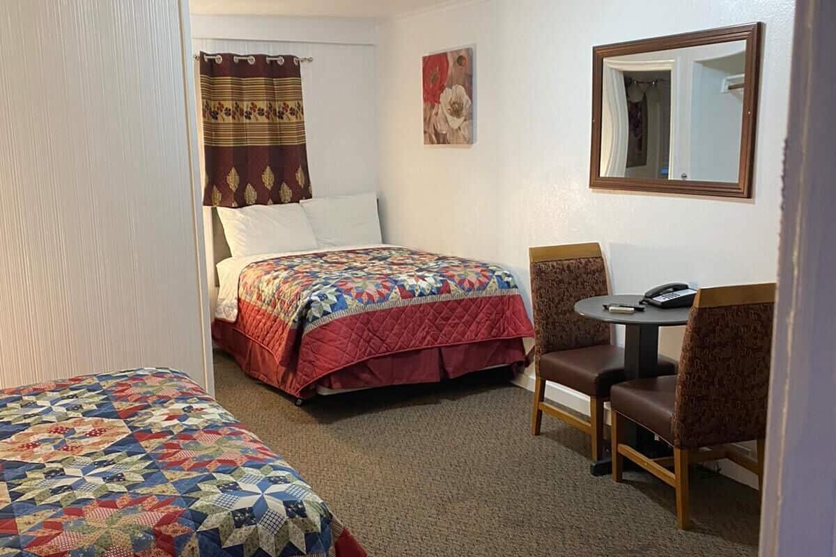 Ett hotellrum med två sängar, ett litet bord med en stol, en spegel och en taklampa.
