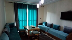Een woonkamer met een zithoek, een eettafel met stoelen en een televisie aan de muur.