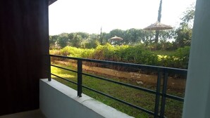 Een balkon met een metalen hekwerk, met uitzicht op een grasveld met een pad en een gebouw in de verte.