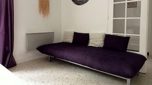 Una habitación con un sofá morado, un reloj de pared y un adorno de macramé.