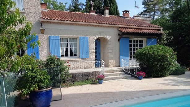 Una casa con piscina, contraventanas azules y plantas en macetas.