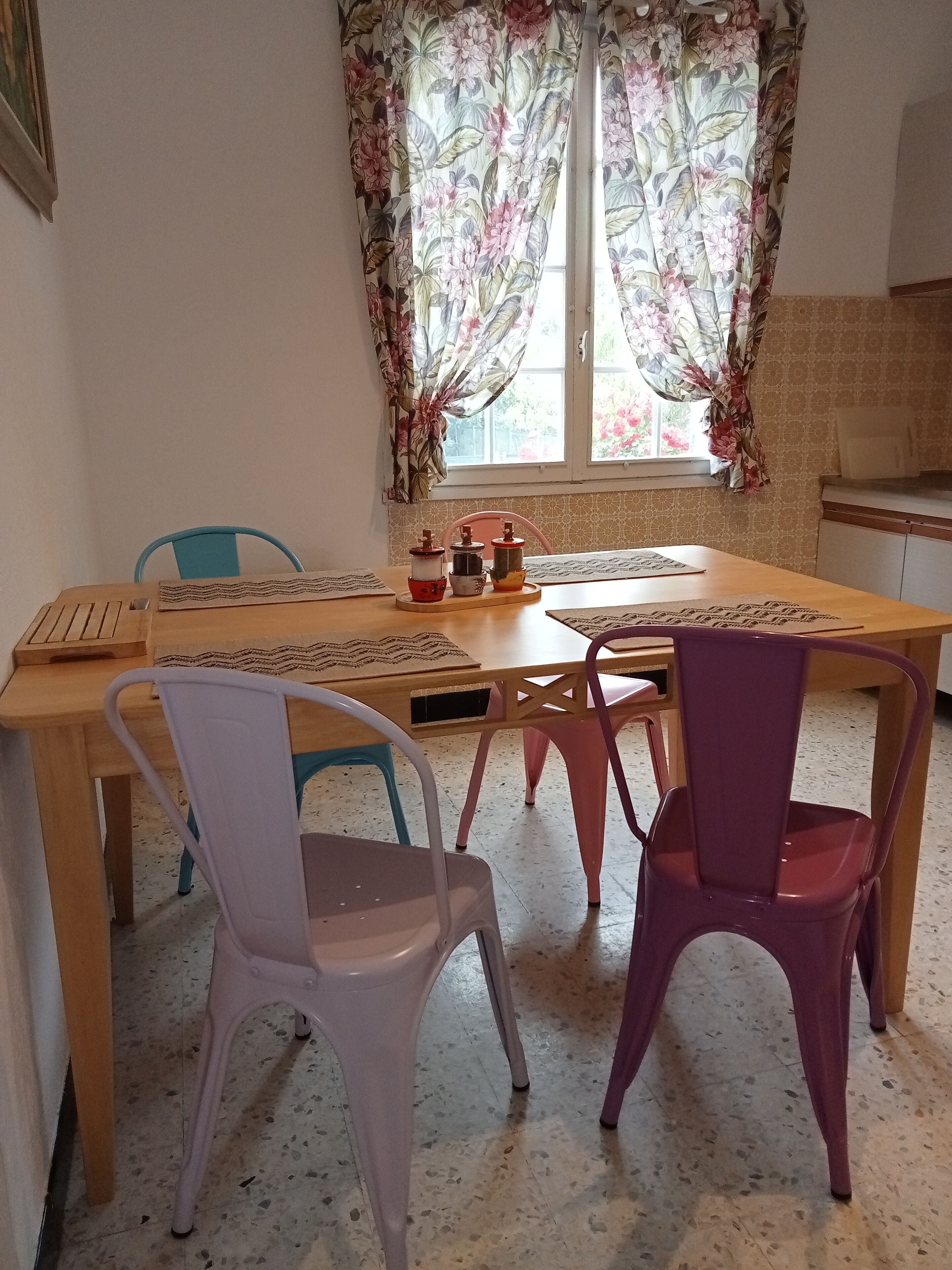 Een eetgedeelte met een houten tafel, twee stoelen en een raam met bloemen gordijnen.