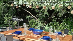 Un área de comedor al aire libre con una mesa de madera dispuesta para cuatro personas, rodeada de sillas de metal.