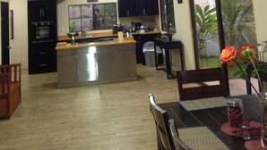 Uma cozinha moderna com armários escuros, uma ilha central e uma área de jantar com mesa e cadeiras.