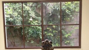 Uma mesa com um pote de cerâmica e dois copos, uma janela com vista para o verde, e uma parede lisa.