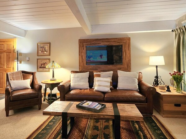 A cozy living room with leather sofas, a coffee table, and a TV mounted on a stone wall.