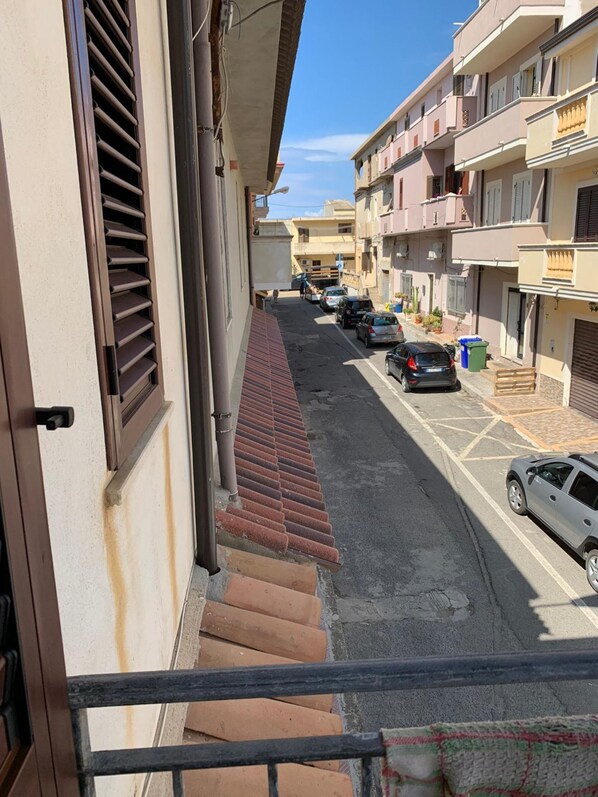 A residential street with parked cars, a tiled sidewalk, and multi-story buildings with balconies.