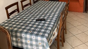 A dining area with a table set for four, surrounded by wooden chairs. There is a sofa against the wall and a ceiling fan above. - Appartamento Telemaco (Le Castella)