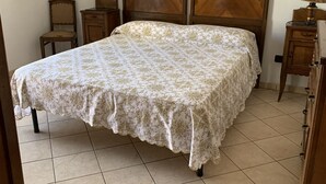 A bedroom with a large bed, wooden headboard, a small bedside table, a chair, and a picture on the wall. - Appartamento Telemaco (Le Castella)