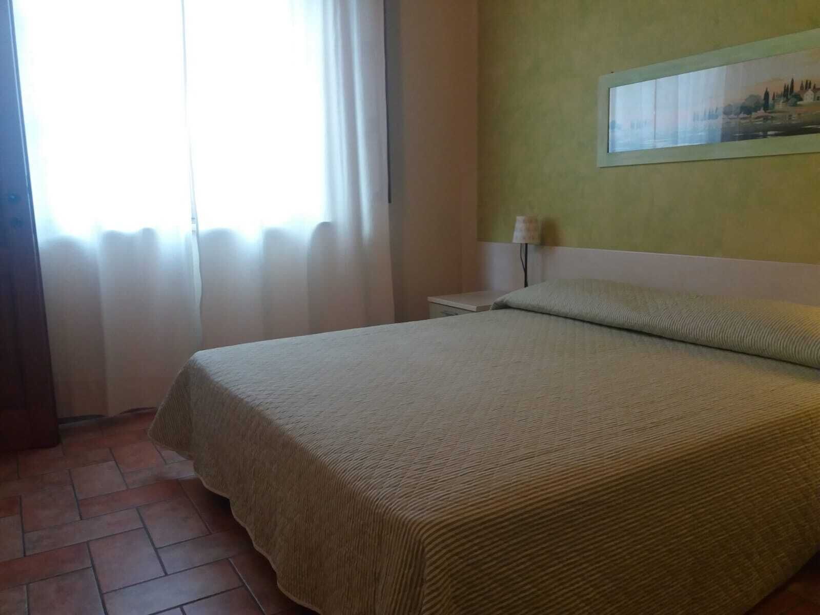 A hotel room with a bed, a nightstand, a lamp, and a painting on the wall.