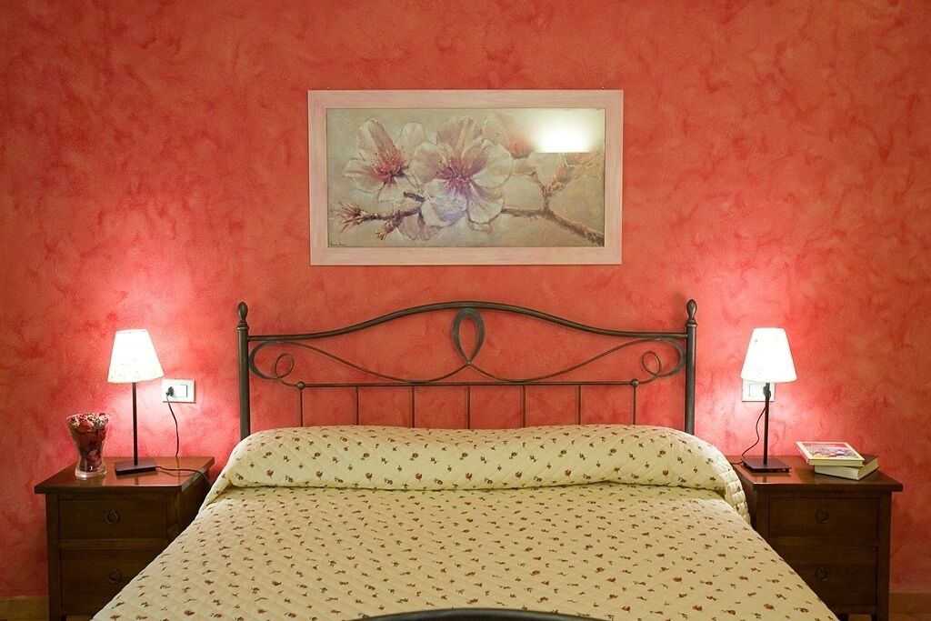 Un dormitorio con una cama, dos mesitas de noche, un buró, una obra de arte floral enmarcada en la pared y una lámpara en cada mesita de noche.