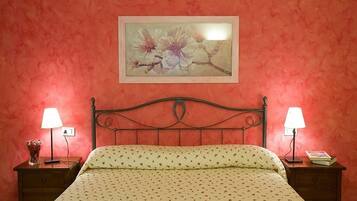 Un dormitorio con una cama, dos mesitas de noche, un buró, una obra de arte floral enmarcada en la pared y una lámpara en cada mesita de noche.
