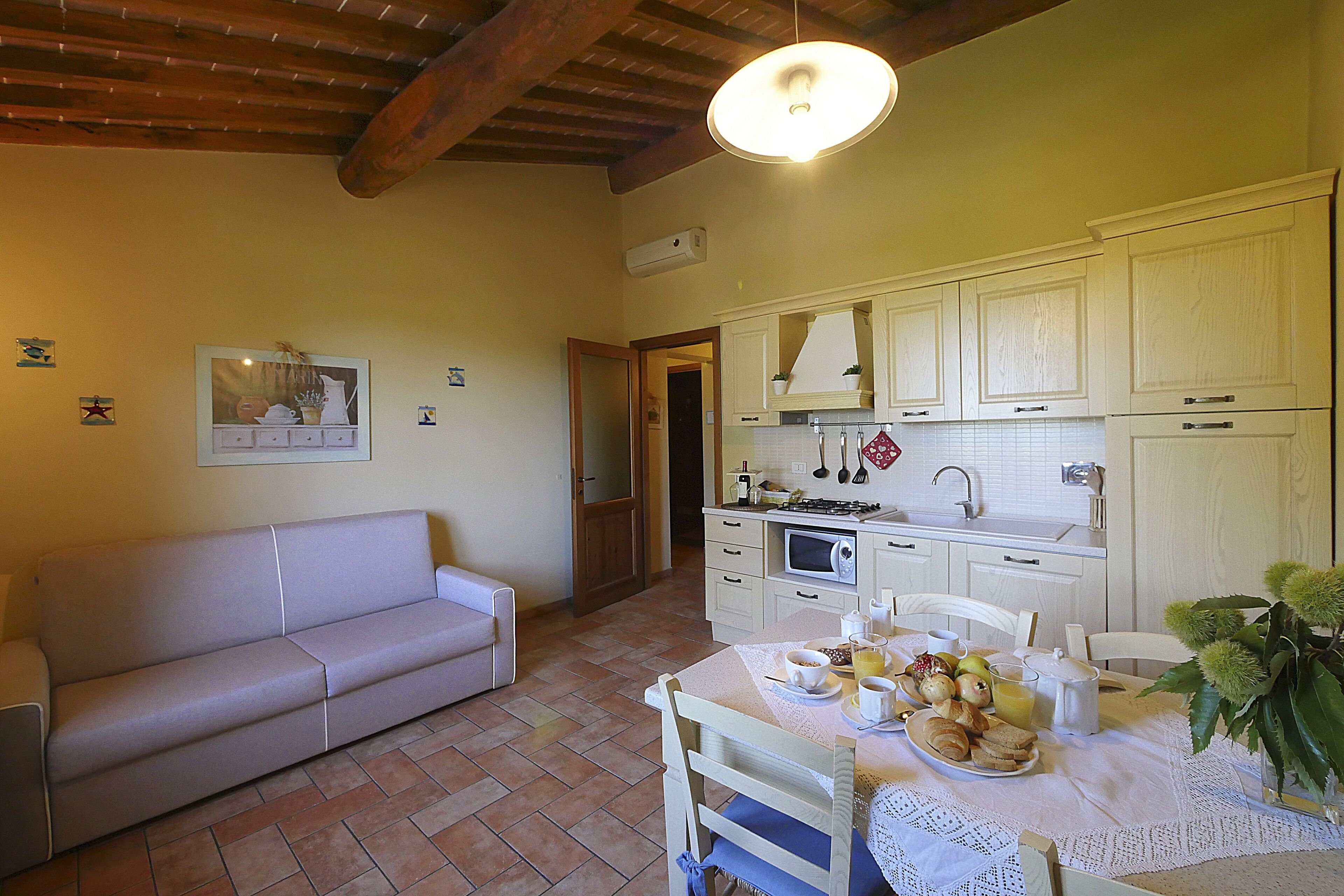 Une cuisine chaleureuse avec une table à manger dressée pour le petit-déjeuner, un canapé et un ventilateur de plafond.