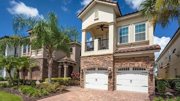 A two-story house with a stone facade, a balcony, and a garage. - Bright Home with Game Room Theater at Reunion (Kissimmee)