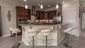 A modern kitchen with a central island, bar stools, stainless steel appliances, and pendant lighting. - Bright Home with Game Room Theater at Reunion (Kissimmee)