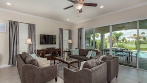 A spacious living room with a flat-screen TV, a wooden entertainment center, and a large sliding glass door leading to an outdoor patio with a pool. - Bright Home with Game Room Theater at Reunion (Kissimmee)