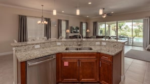A kitchen with granite countertops, wooden cabinets, and a built-in dishwasher. - Bright Home with Game Room Theater at Reunion (Kissimmee)