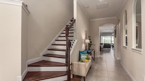A home interior with a wooden staircase, a hallway leading to a dining area, and a view of the outdoors. - Bright Home with Game Room Theater at Reunion (Kissimmee)