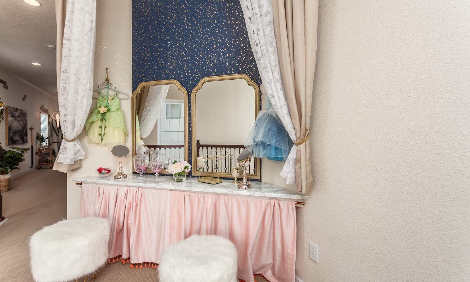 A vanity with a marble countertop, two mirrors, and a pink skirted bench.