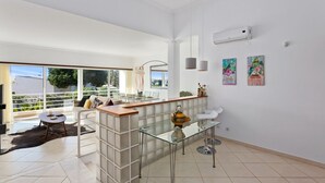 A modern living room with a glass coffee table, a sofa, and a dining area with a glass partition. - Ocean Villas-Villa Sol (Guia)