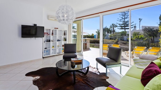 A modern living room with a glass door leading to an outdoor area with yellow chairs. - Ocean Villas-Villa Sol (Guia)