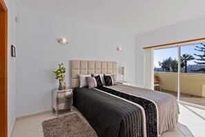 A bedroom with a large bed, a nightstand, a dresser, and a view of the outside. - Ocean Villas-Villa Sol (Guia)