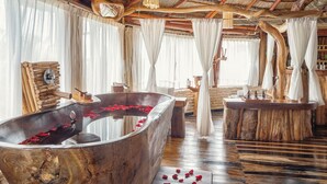 Un baño rústico con una bañera de madera grande, muebles de madera y una pared de piedra natural.