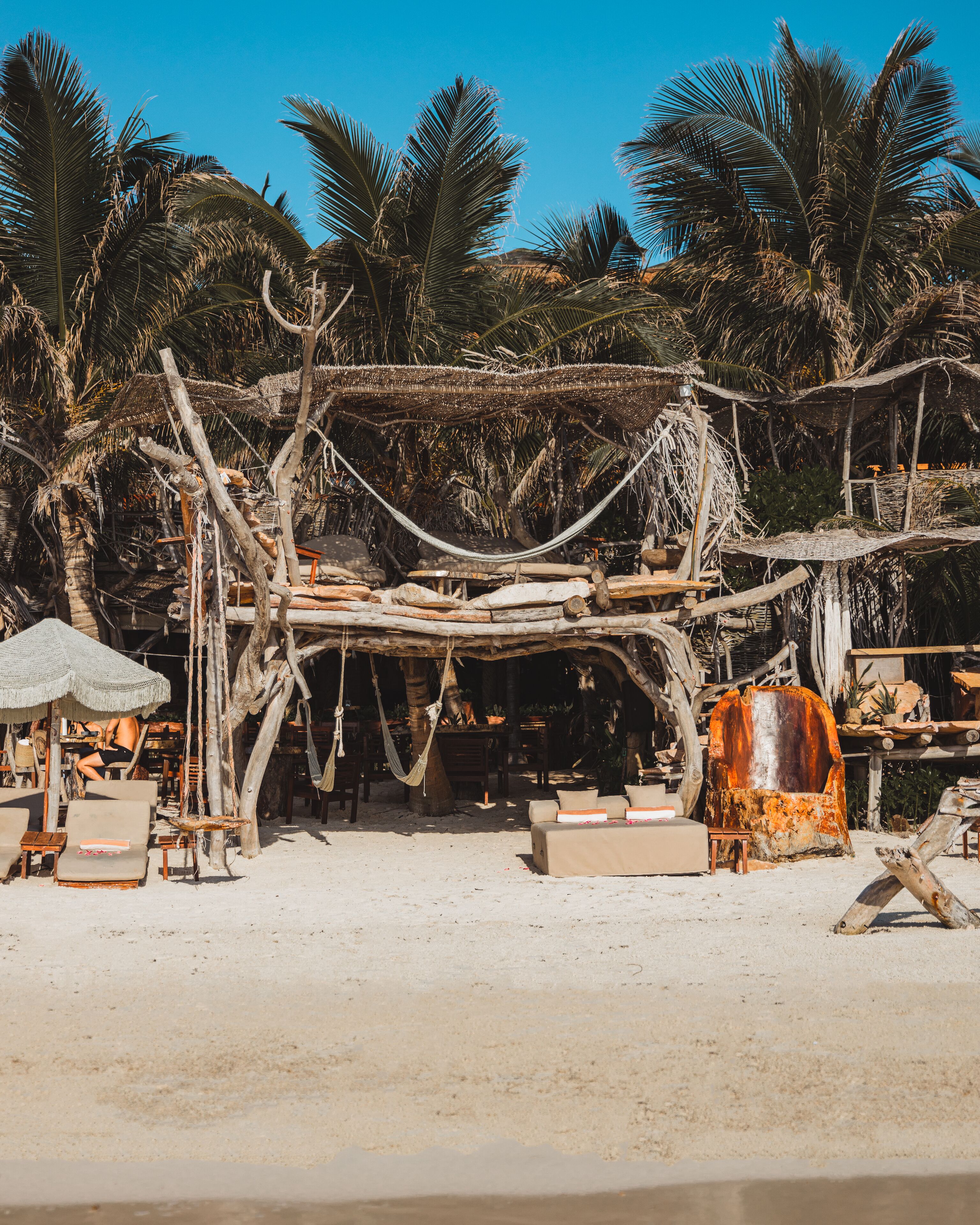 Un décor de plage avec une structure en bois rustique, des hamacs et des chaises longues.
