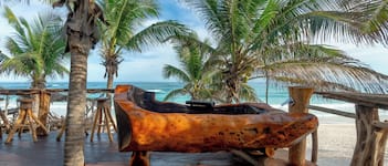 A wooden boat sculpture on a wooden deck with palm trees and a beach view.