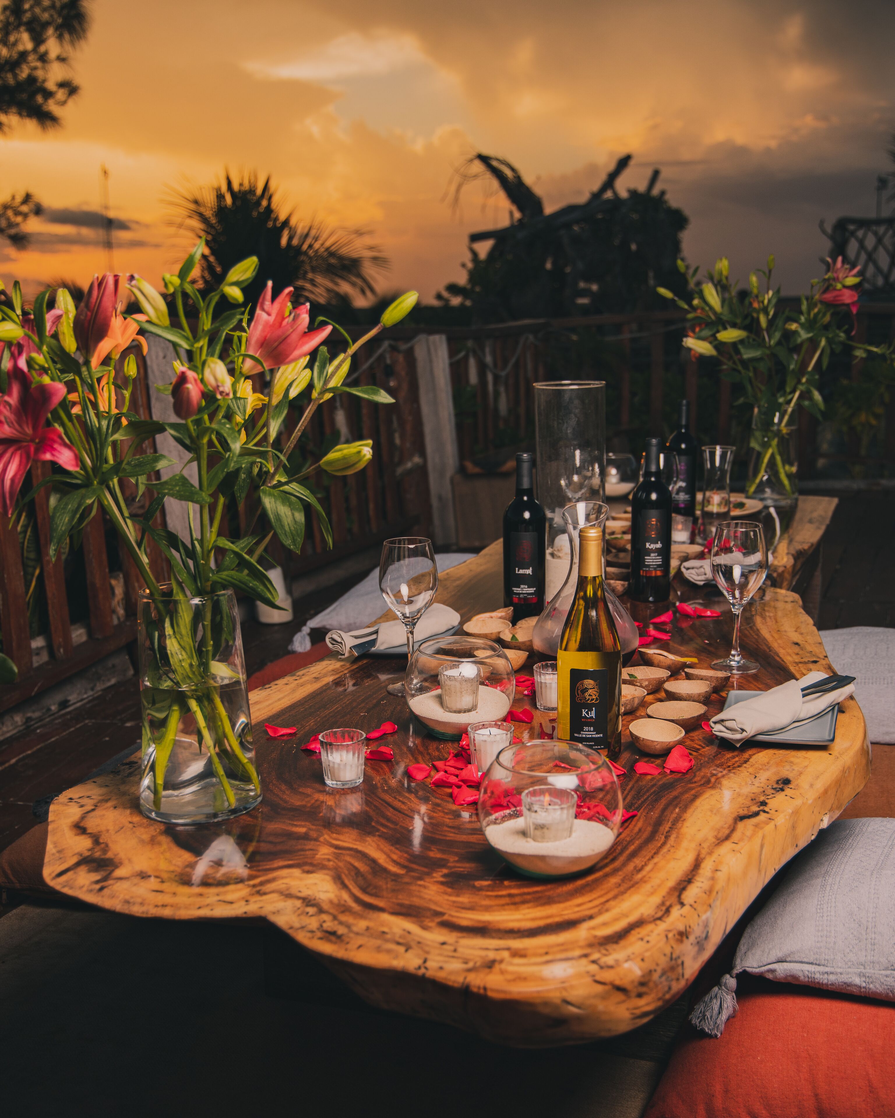 A wooden table set with wine glasses, bottles, and a centerpiece of flowers.