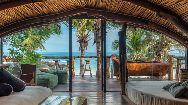 Una habitación frente al mar con techo de madera curvada, un amplio ventanal con vistas al océano y un banco de madera junto a la ventana.