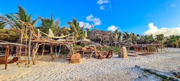 Una playa con estructuras de madera, incluyendo columpios y sombrillas, rodeada de palmeras.